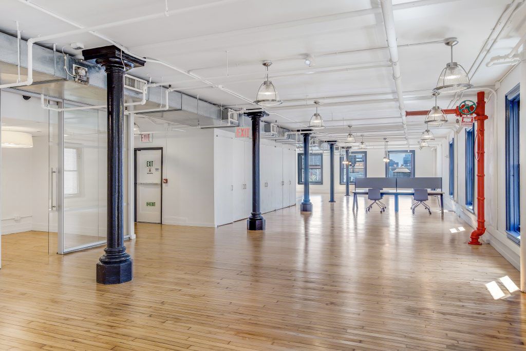 Open loft floor with cast-iron columns, exposed ductwork and a glass-front room